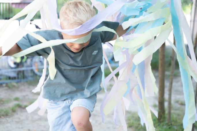 Kind läuft durch bunte Stoffbänder – lebendige Kita-Fotografie statt steifer Reihenbilder